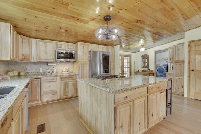 kitchen featuring hanging light fixtures, a kitchen island, appliances with stainless steel finishes, and light brown cabinets