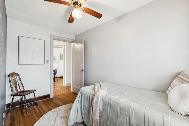 bedroom with dark hardwood / wood-style flooring, ceiling fan, and a textured ceiling