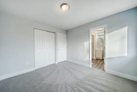 unfurnished bedroom with ensuite bath, carpet flooring, and a closet