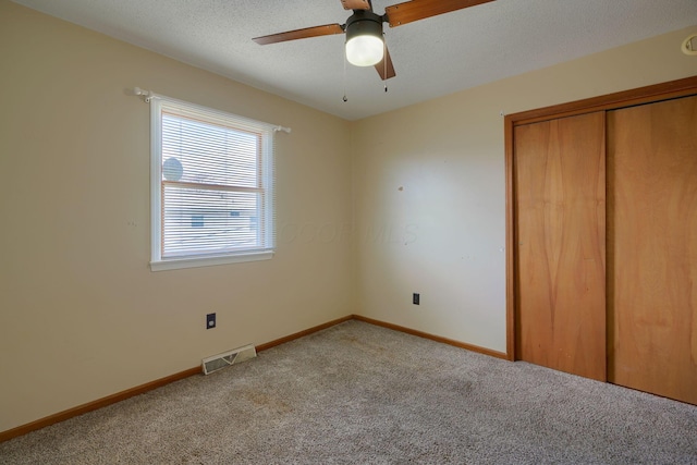 unfurnished bedroom featuring ceiling fan, light colored carpet, a closet, and a textured ceiling