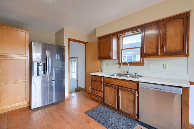 kitchen with appliances with stainless steel finishes, sink, a textured ceiling, and light wood-type flooring