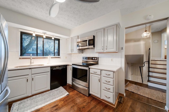 kitchen with dark wood-type flooring, stainless steel appliances, sink, and hanging light fixtures