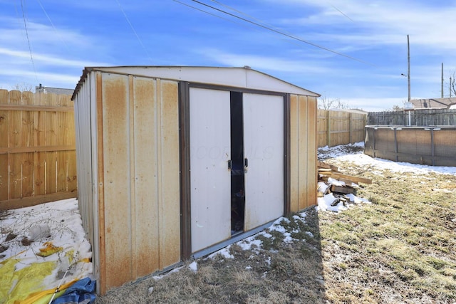 snow covered structure with a storage shed, an outbuilding, a fenced backyard, and a fenced in pool