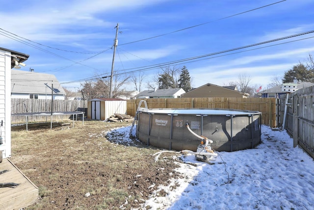 yard covered in snow featuring a fenced in pool, a fenced backyard, a trampoline, a storage unit, and an outdoor structure