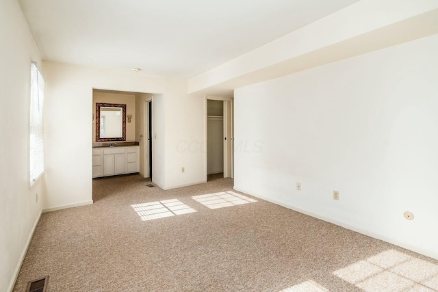 empty room with sink, light colored carpet, and a healthy amount of sunlight