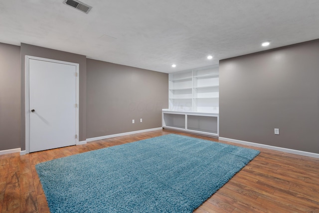 spare room with built in shelves and wood-type flooring