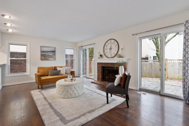 living room featuring a brick fireplace, a textured ceiling, and dark hardwood / wood-style flooring