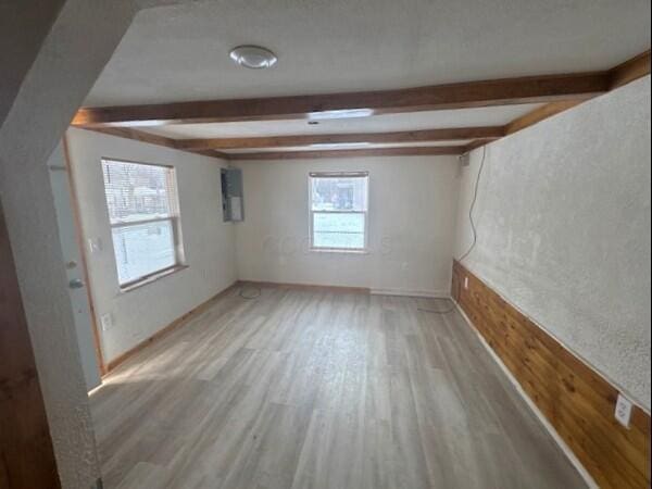 unfurnished room with beam ceiling, electric panel, and light wood-type flooring