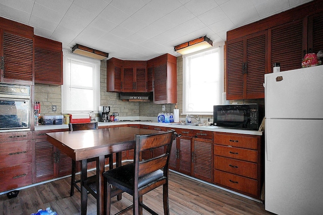 kitchen featuring dark hardwood / wood-style floors, sink, oven, backsplash, and white refrigerator