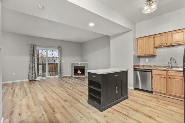 kitchen with sink, dishwasher, backsplash, a fireplace, and light hardwood / wood-style floors