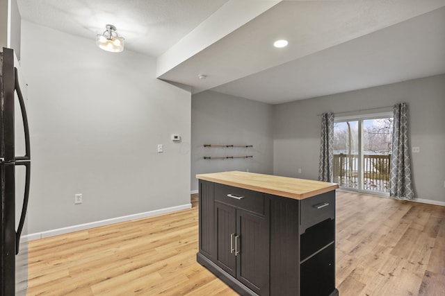 kitchen with wood counters, dark brown cabinets, black refrigerator, and light hardwood / wood-style floors