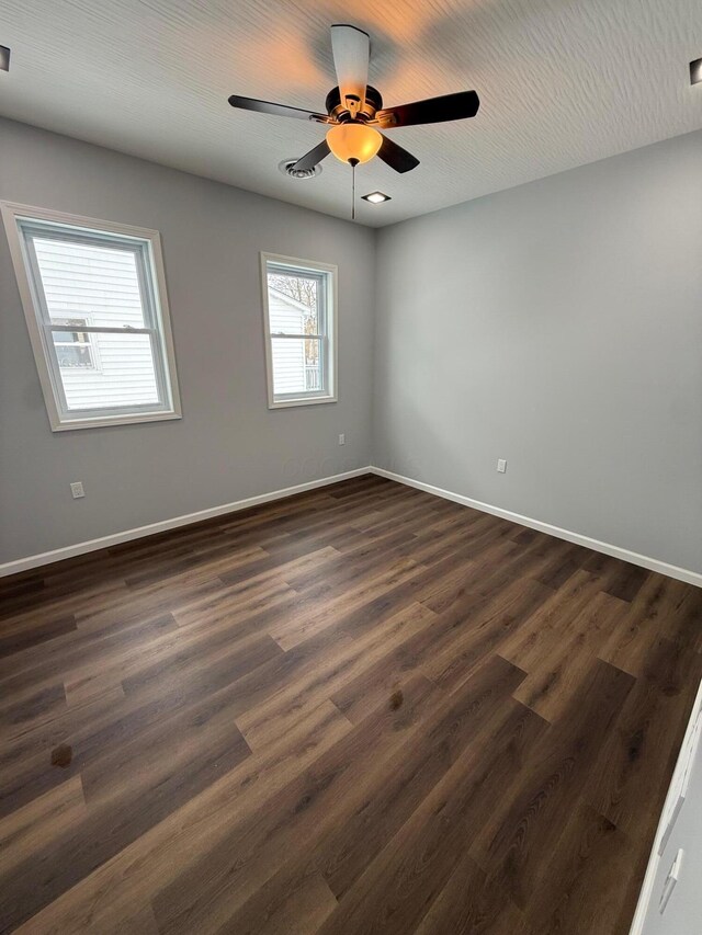 unfurnished room with dark wood-type flooring, a ceiling fan, and baseboards