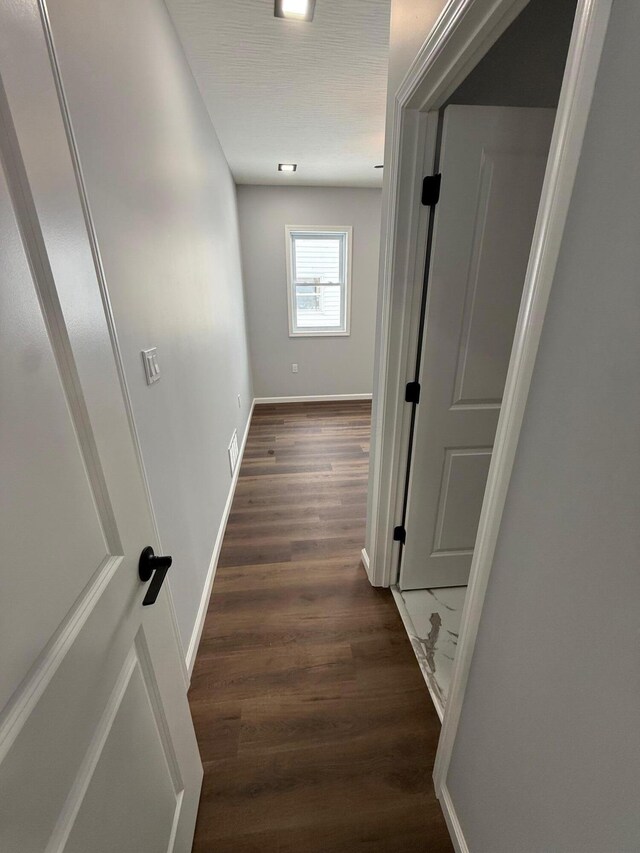 hallway with dark wood-type flooring, visible vents, and baseboards