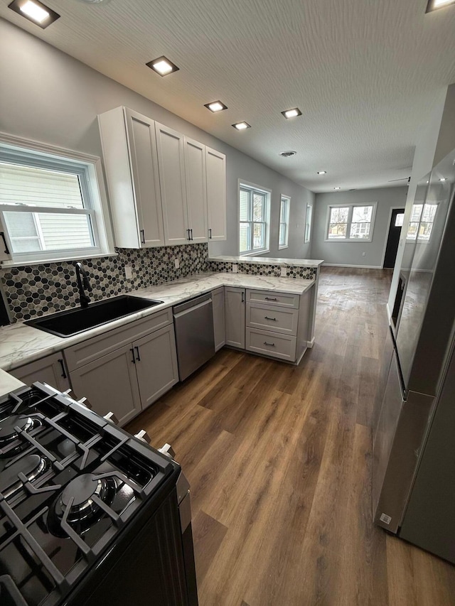 kitchen with a sink, black gas stove, open floor plan, dishwasher, and dark wood finished floors