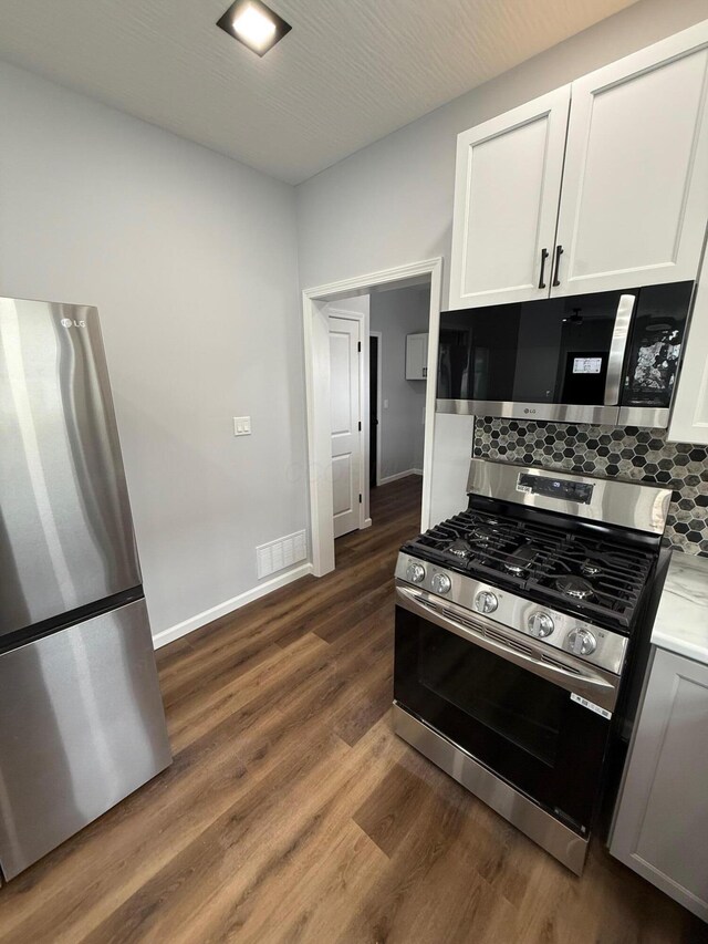 kitchen with tasteful backsplash, light countertops, appliances with stainless steel finishes, dark wood-type flooring, and white cabinetry