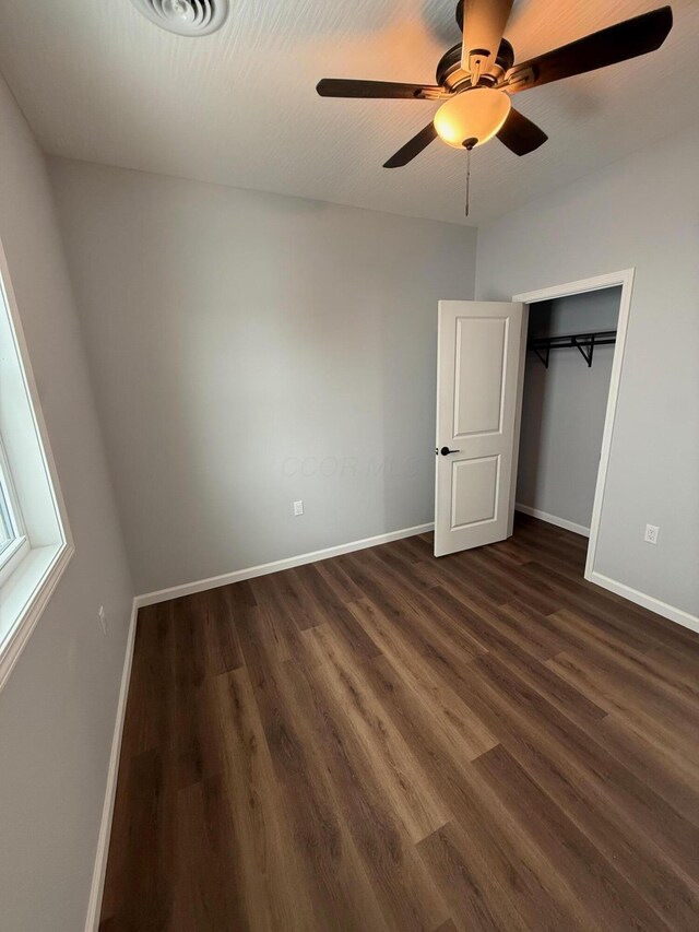 unfurnished bedroom featuring ceiling fan, a closet, baseboards, and dark wood-style flooring