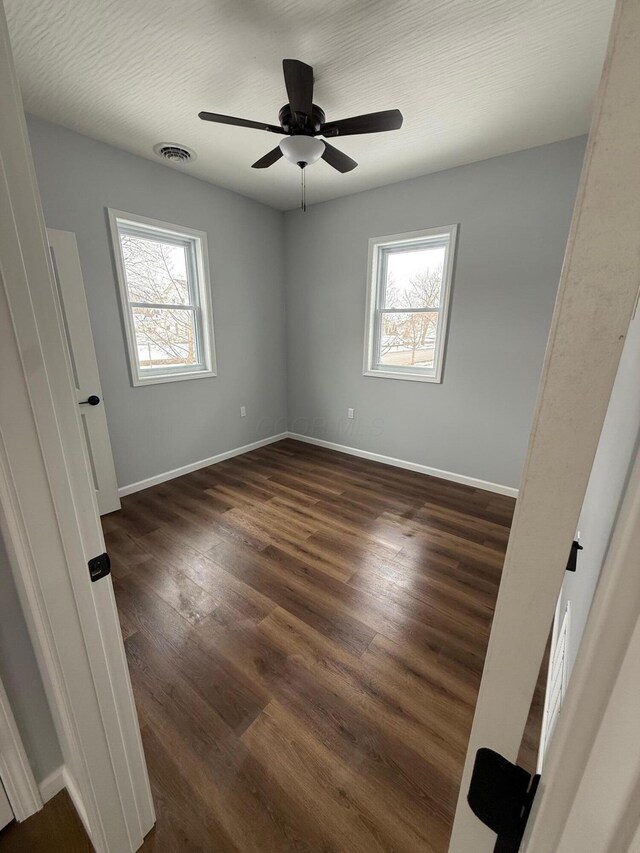 unfurnished bedroom with dark wood-style floors, visible vents, baseboards, and a ceiling fan