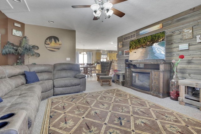 living area with a ceiling fan, carpet, a glass covered fireplace, and wood walls