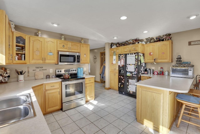 kitchen featuring a breakfast bar, a sink, light countertops, appliances with stainless steel finishes, and glass insert cabinets