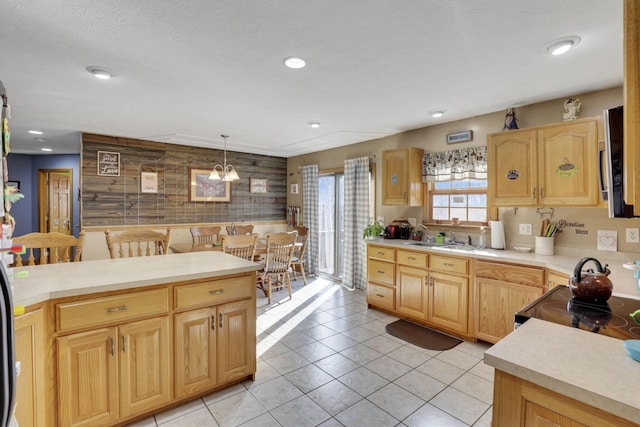 kitchen featuring light countertops, hanging light fixtures, light brown cabinetry, wood walls, and a sink