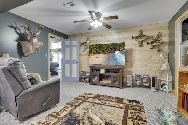 carpeted living room with a ceiling fan, visible vents, and wood walls