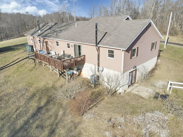 exterior space with roof with shingles, a yard, an attached garage, central AC, and a wooden deck