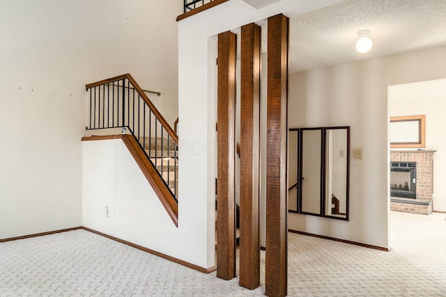 stairs with a brick fireplace, a textured ceiling, and carpet flooring