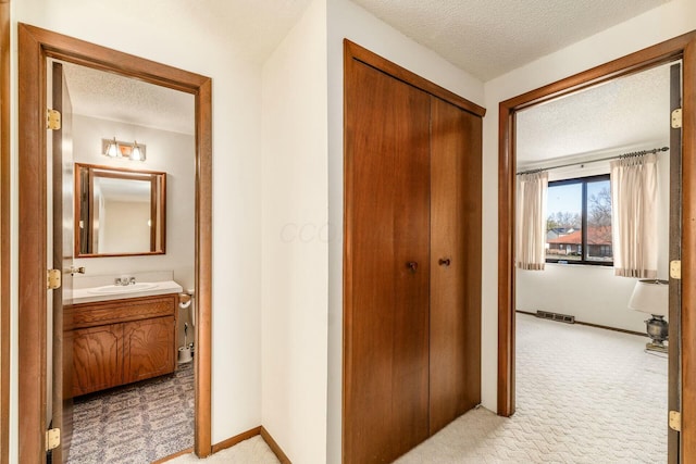 hall featuring light carpet, sink, and a textured ceiling