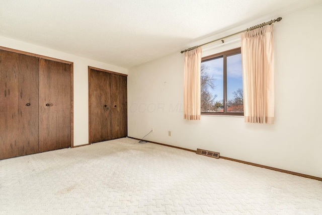 unfurnished bedroom featuring two closets, a textured ceiling, and carpet flooring