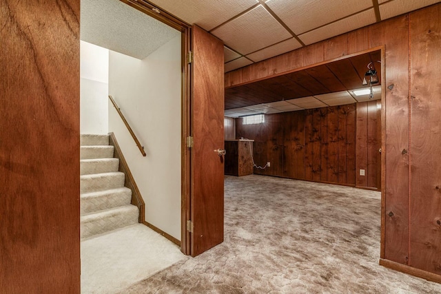 basement with wooden walls, light colored carpet, and a paneled ceiling