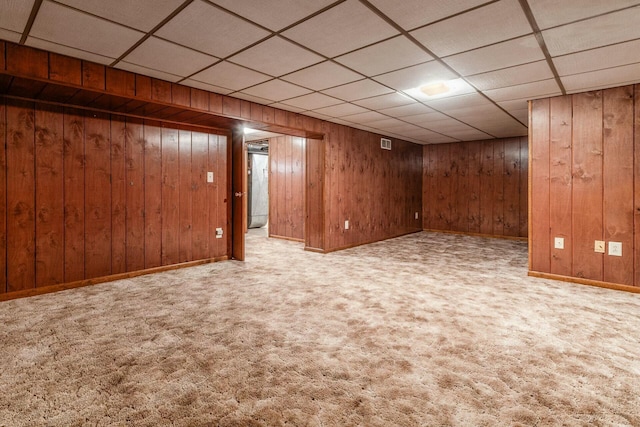 basement with light colored carpet, wooden walls, and a drop ceiling