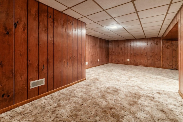 basement featuring a paneled ceiling, wooden walls, and carpet