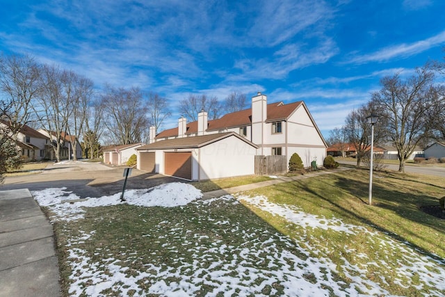 view of snowy exterior featuring a garage, an outbuilding, and a lawn