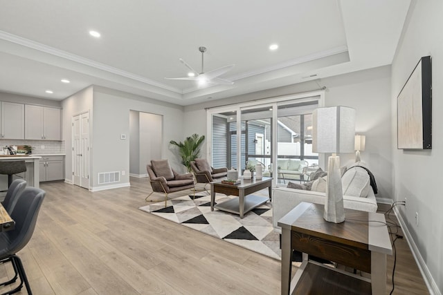 living room with ceiling fan, ornamental molding, a raised ceiling, and light hardwood / wood-style floors