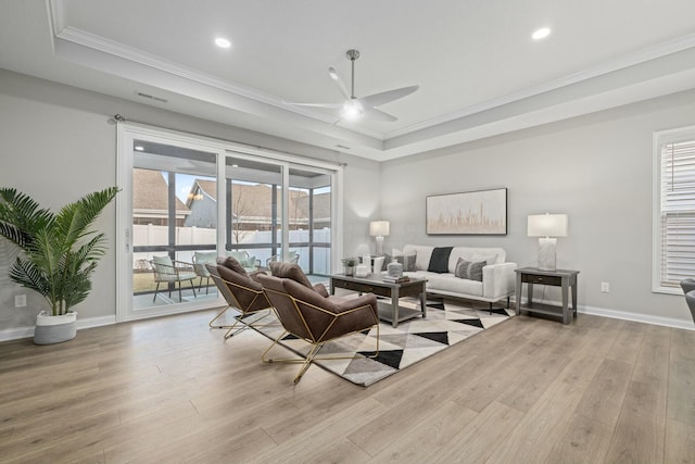 living room with a raised ceiling, ornamental molding, plenty of natural light, and light hardwood / wood-style floors