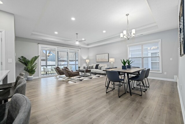 dining space with a tray ceiling, ceiling fan with notable chandelier, ornamental molding, and light wood-type flooring