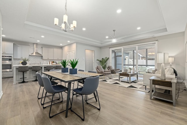 dining area featuring a notable chandelier, a tray ceiling, light hardwood / wood-style flooring, and ornamental molding