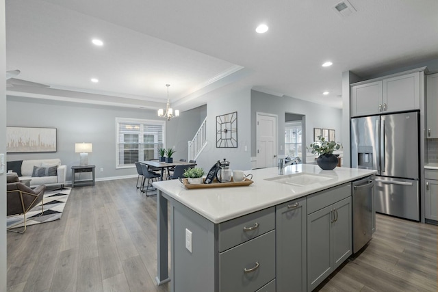 kitchen with gray cabinets, appliances with stainless steel finishes, a kitchen island with sink, and sink