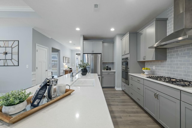 kitchen featuring stainless steel appliances, gray cabinets, sink, and wall chimney range hood