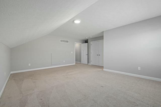 bonus room with vaulted ceiling, light colored carpet, and a textured ceiling