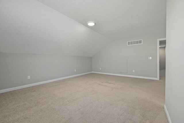 bonus room with vaulted ceiling, light colored carpet, and a textured ceiling