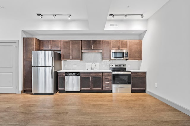 kitchen with dark brown cabinetry, sink, light hardwood / wood-style flooring, stainless steel appliances, and backsplash