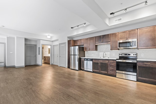 kitchen featuring appliances with stainless steel finishes, rail lighting, backsplash, light hardwood / wood-style floors, and dark brown cabinets