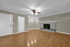 unfurnished living room with ceiling fan, wood-type flooring, a brick fireplace, and ornamental molding