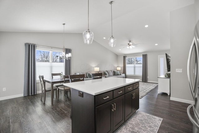 kitchen with lofted ceiling, dark hardwood / wood-style flooring, a kitchen island, pendant lighting, and ceiling fan with notable chandelier