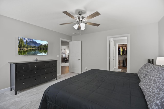 bedroom with a spacious closet, light colored carpet, ceiling fan, and a closet