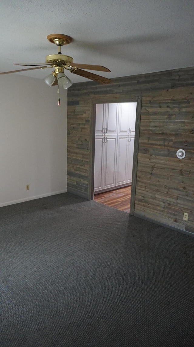 unfurnished room with ceiling fan, a textured ceiling, dark carpet, and wood walls