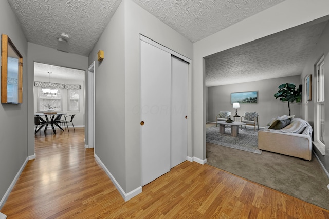 hall with an inviting chandelier, a textured ceiling, and light wood-type flooring