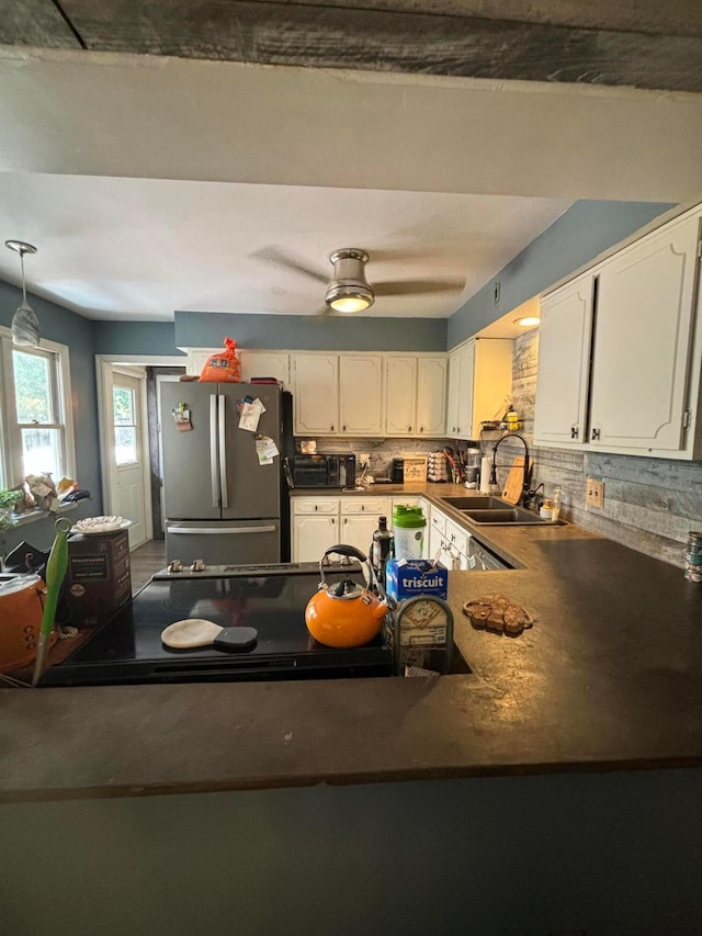 kitchen with sink, stainless steel fridge, white cabinetry, tasteful backsplash, and decorative light fixtures