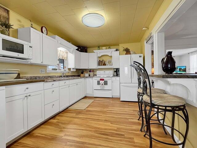 kitchen with white cabinetry, a healthy amount of sunlight, white appliances, and light hardwood / wood-style floors